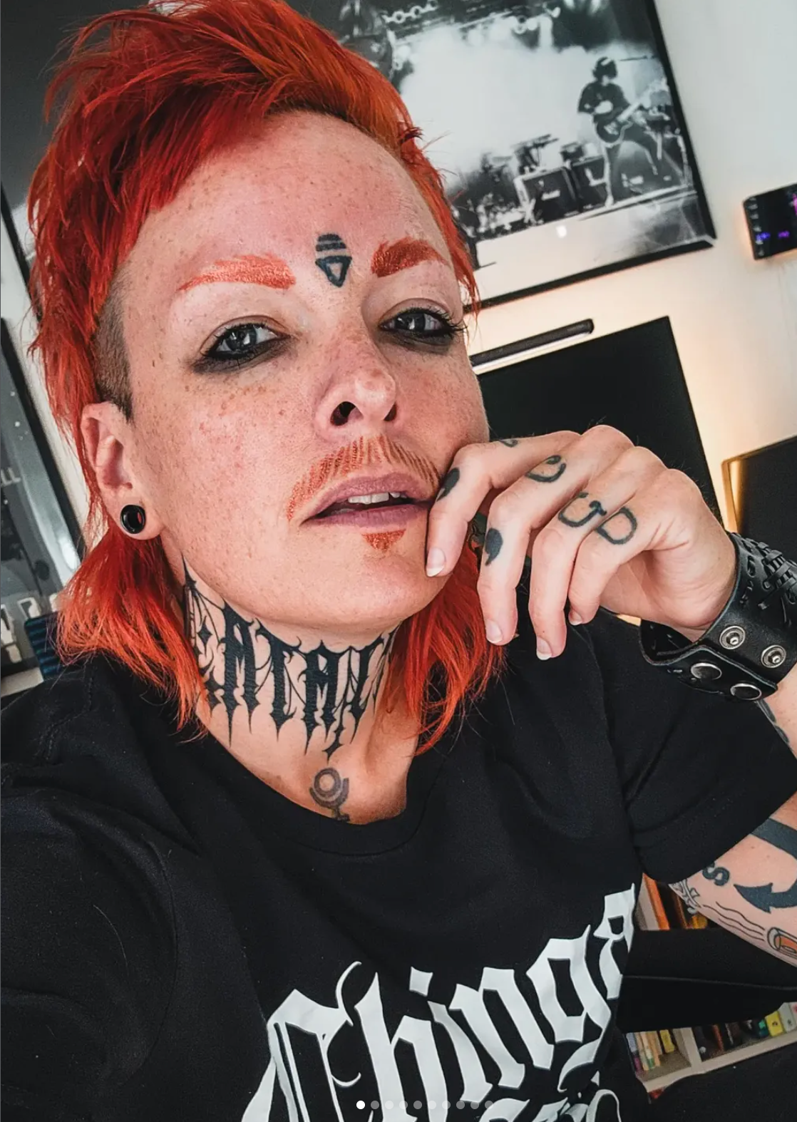 Ro in a selfie with red hair, tattoos, and a black band shirt.